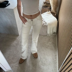 Vita bootcut jeans från Nelly - Säljer ett par vita bootcut jeans från Nelly med snygga detaljer och klassiska fickor. Jeansen har låg midja och markerade sömmar, samt en ikonisk M-detalj på bakfickan. Perfekta för en trendig och fräsch look.
