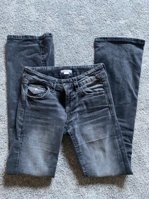 Mörkgrå bootcut jeans  - Snygga mörkgrå bootcut jeans, broderade detaljer på bakfickorna. Jeansen har fem fickor, knappgylf och kontrastsömmar. Perfekta för en avslappnad och trendig look.