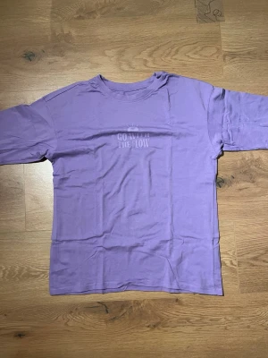 Lila t-shirt från 4F med tryck - Lila t-shirt från 4F med texten 'Go With The Flow' tryckt framtill. Klassisk rund halsringning och korta ärmar. Perfekt för dig som gillar en chill och färgglad stil.
