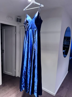Marinblå balklänning i satin - Elegant marinblå långklänning med smala axelband och v-ringad urringning. Klänningen har en glansig satinfinish som ger ett lyxigt intryck och ett flytande fall. Perfekt för balen eller bröllopet! Jag har använt den och haft på mig den en enda gång och det var min bal i nian. Nypris är ca 3000kr från företaget Dressly
