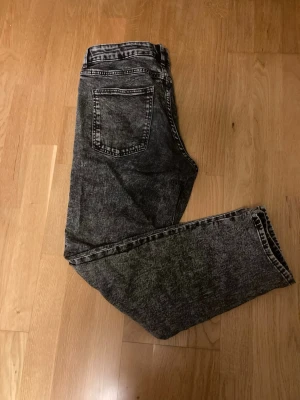 Svarta acid wash jeans raka ben - Säljer ett par svarta acid wash jeans med raka ben och klassisk femficksmodell. Jeansen har hög midja och cool tvätt som ger en retrovibe. Tillverkade i bomull för skön känsla och slitstark kvalitet. Perfekta för dig som gillar en avslappnad men trendig stil.