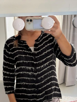 Svart kofta med vita ränder - Säljer en svart kofta med vita, ojämna ränder och lite ruffig textur. Koftan har trekvartsärmar och rak passform. Perfekt att slänga på sig över en topp för en avslappnad men snygg look.