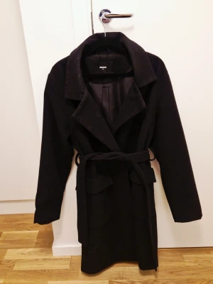 Svart kappa i ullmix - Använd men i bra skick. Har ett litet hål i ena fickan se bild. Utöver det så är den hel och ren. 