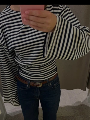 Randig topp från Gina Tricot - Säljer en svartvit randig topp från Gina Tricot. Toppen har vida långärmar och en tight passform i midjan. Perfekt för dig som gillar trendiga och bekväma plagg med lite edge.