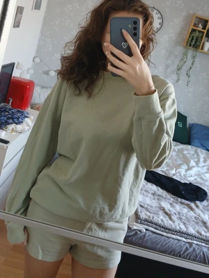 Ljusgrönt sweat-set - Mysigt loungewear-set i ljusgrön färg med långärmad sweatshirt och matchande shorts. Perfekt för att chilla hemma. Materialet ser ut att vara mjukt bomull eller bomullsblandning. Enkel och avslappnad design utan synliga loggor.