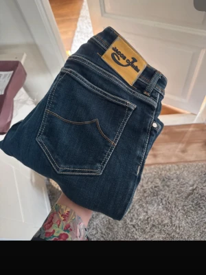 Mörkblå jeans från Jacob Cohen - Snygga mörkblå jeans från Jacob Cohen med klassisk femficksmodell och kontrastsömmar. Jeansen har en patch i mockaimitation med logga bak i midjan och är tillverkade i ett mjukt denimtyg. Perfekta för en trendig och avslappnad look.