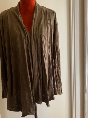Olivgrön lös kofta utan knappar M - Långärmad kofta med en avslappnad passform och en öppen design framtill. Koftan har en draperad krage som ger en mjuk och elegant look. Den är designad för att vara bekväm och mångsidig, perfekt för lager-på-lager eller som ett lätt ytterplagg. 95% viskos 5% elastan  Inga bilder när den sitter på mig! Katter finns i hemmet!