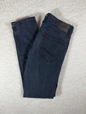 Lee Luke jeans W30 - Snygga mörkblå jeans från Lee med klassisk femficksmodell och raka ben. Jeansen har en diskret Lee-logga på bakfickan och är tillverkade i mjukt denimtyg. Perfekta för en avslappnad och stilren look.