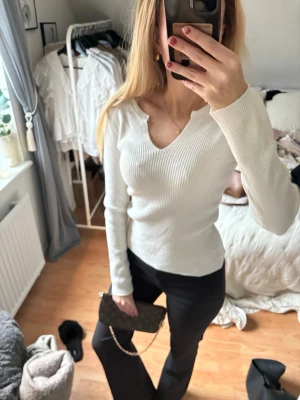 Vit ribbad långärmad topp - Säljer en vit ribbad långärmad topp med v-ringning och snygg passform. Perfekt för dig som gillar stilrena och enkla plagg som ändå har lite edge. Toppen är figurnära och har en modern look som passar till många outfits.