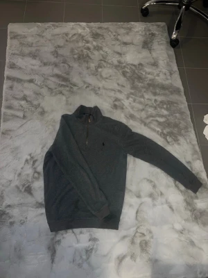 Grå quarter zip från Polo Ralph Lauren - Mysig grå tröja med quarter zip och hög krage från Polo Ralph Lauren. Klassisk broderad logga på bröstet och ribbade muddar vid ärmslut och nederkant. Perfekt för lager på lager och enkel att matcha med jeans eller chinos.
