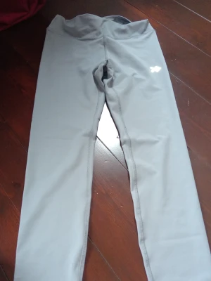 Grå träningsbyxor  - Snygga grå träningsbyxor med hög midja och stretchigt material. Perfekta för träning eller chill, med diskret logga på låret. Tight passform och mjukt tyg som sitter skönt hela dagen.