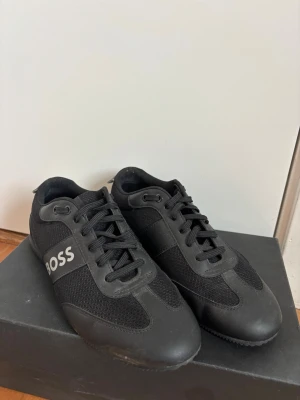 Svarta sneakers från BOSS - Stilrena svarta sneakers från BOSS, svarta snören och tydlig BOSS-logga på sidan. Perfekta för dig som gillar en clean och sportig look. Använda fåtal gånger och endast inomhus! Pris kan diskuteras🙌🏼