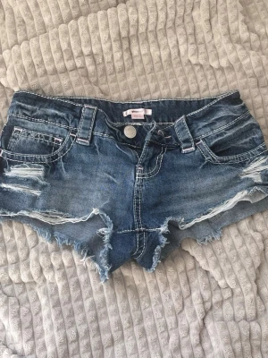 Lowwaist shorts från Gina Tricot, "14+ xtra low denim shorts" - Mörkblåa jeansshorts från Gina Tricot, korta och låg i midjan med detaljer på fickorna samt inslag av rosa detaljer. Storlek xxs. Säljer eftersom de är för små för mig. Oanvända.