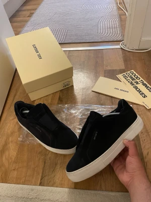 Svarta sneakers från Axel Arigato - Stilrena svarta sneakers från Axel Arigato med tjock vit sula och minimalistisk design. Skorna har en låg silhuett och är tillverkade i mocka med diskret logga på sidan. Perfekta för dig som gillar clean och modern stil.storlek 42 passar 43