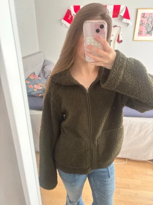 Olivgrön teddyjacka  - Mysig olivgrön teddyjacka med dragkedja framtill och bred krage som man kan vika ner