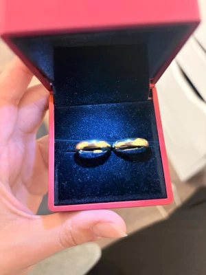 Guldfärgade släta ringar i ask - Två stilrena guldfärgade ringar med klassisk, slät design. Levereras i en elegant röd ringask med svart sammet inuti. Perfekta för dig som gillar enkel och tidlös stil. Materialet ser ut att vara metall med guldfinish.