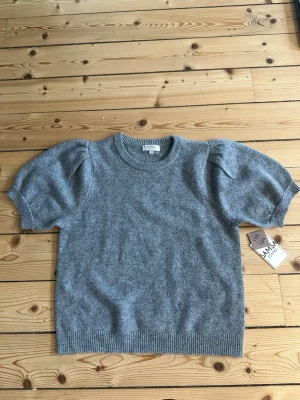Grå puffärm stickad tröja SAMSA - Säljer en grå stickad tröja från SAMSA med puffärmar och rund hals. Tröjan har korta ärmar och ribbade muddar vid ärmslut och nederkant. Perfekt för dig som gillar en trendig och mysig look.