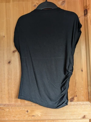 Svart basic t-shirt i bomull - En enkel svart t-shirt med korta ärmar och rund hals. Tillverkad i mjuk bomull som känns skön mot huden. Passformen är normal och modellen är klassisk utan tryck eller mönster. Perfekt att matcha med jeans eller kjol.