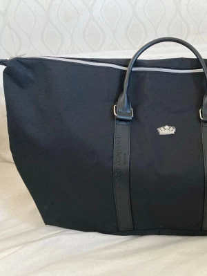 Svart Dolce & Gabbana weekendväska - Stor svart weekendväska från Dolce & Gabbana Beauty med stilren design, dubbla handtag i skinn och silverfärgad kron-detalj framtill. Väskan har dragkedja upptill och är tillverkad i slitstark polyester.