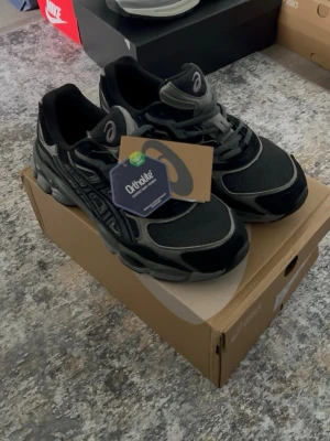 Asics Gel - Snygga svarta Asics sneakers med grå detaljer. Ovandelen är i mesh och syntetiskt skinn för både stil och komfort. Klassisk Asics-logga på sidan och Ortholite-innersula för extra support. Perfekta för dig som gillar sportig och trendig look.