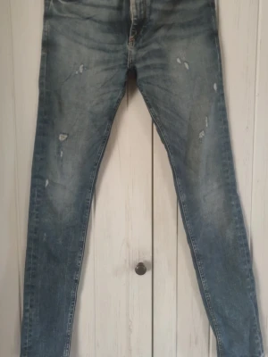 Blå slitna skinny jeans - Snygga blå skinny jeans med slitningar och tvättade detaljer. Jeansen har klassisk femficksdesign och smal passform som sitter tight längs benen. Perfekta för en avslappnad och trendig look.