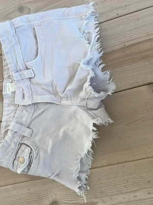 Ljusa fransiga shorts från Gina Tricot - Säljer ett par ljusa rosa denimshorts från Gina Tricot med råa, fransiga kanter och klassisk femficksmodell. Shortsen har bälteshällor och knappgylf. Perfekta för varma dagar och en avslappnad look.