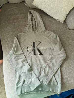 Calvin Klein Jeans Hoodie | Grå | S - ▫️ Calvin Klein Jeans hoodie i grått ▫️ Storlek: S ▫️ Mjuk och bekväm passform ▫️ Klassisk CK-logga framtill ▫️ Perfekt till både vardag, skola och loungewear    📸 Skickar gärna fler bilder, närbilder, mått eller passformsbilder vid intresse.                                    💬 Hör gärna av dig om du har frågor!