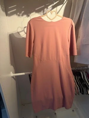 Rosa kort klänning med dragkedja - Söt rosa kortklänning med halvlånga ärmar och rund halsringning. Klänningen har en markerad midja och dragkedja i ryggen för enkel påklädning. Perfekt för dig som gillar enkel men stilren design.