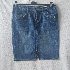 Blå jeanskjol från polo Ralph Lauren W43 L54 - Säljer en klassisk blå jeanskjol från True Religion med fem fickor, bälteshällor och knappgylf. Kjolen har en rak passform och slitna detaljer för en cool look. Perfekt till sneakers eller boots.