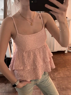 Rosa volangtopp  - Säljer en ljusrosa topp med smock och dubbla volanger. Toppen är ärmlös med tunna axelband och har en luftig, flowy passform. Axelbanden kan justeras. Använd ett fåtal gånger. Hör av dig vid frågor🤗