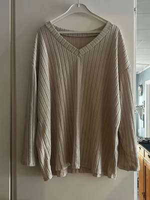 Beige oversized stickad tröja - Säljer en beige oversized stickad tröja med v-ringning och breda ribbade ränder. Tröjan har långa, lösa ärmar och ett mjukt, följsamt material som ger en avslappnad look. Perfekt för lager på lager och chill dagar.