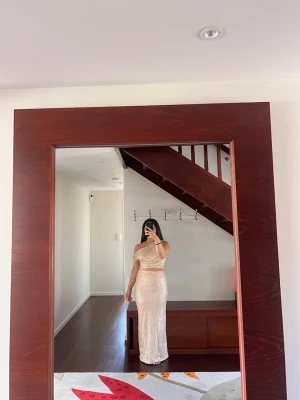 Champagnefärgad glittrig långklänning - Säljer en elegant champagnefärgad långklänning med glittrigt tyg och oneshoulder-design. Klänningen har en figurnära passform och är perfekt för dig som vill sticka ut på nästa stora event. Materialet känns lyxigt och skimrar snyggt i ljuset.