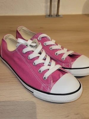 Rosa låga sneakers med vita detaljer - Snygga rosa sneakers i canvas med vita gummisulor och tåhätta. Skorna har vita skosnören och silverfärgade öljetter. Klassisk låg modell som passar perfekt till jeans eller shorts. Helt oanvända. 