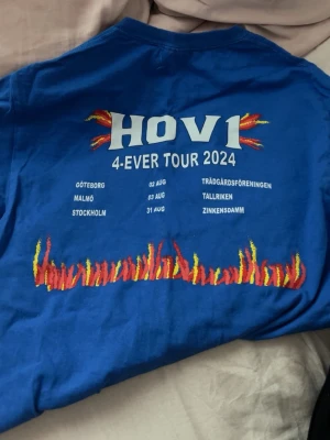 Blå Hov1 4-Ever Tour 2024 t-shirt - Säljer en blå t-shirt med tryck från Hov1s 4-Ever Tour 2024. Baksidan har turnétryck med eld-detaljer och städer, framsidan har en liten röd krona. Har aldrig använt den❤️