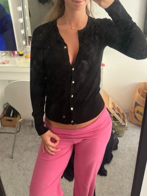 Svart kofta med pärlknappar - Snygg svart kofta med långa ärmar och pärlknappar framtill. Figurnära modell med stretchigt material. Perfekt att styla till både jeans och kjol.
