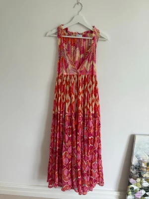 Färgglad långklänning med mönster - En långklänning med mixade mönster i rosa, rött och beige. Klänningen har v-ringning, ärmlös design och ett flowigt fall. Perfekt för sommarens varma dagar.