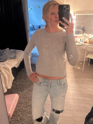 Ljusgrå långärmad topp - Säljer en enkel och stilren ljusgrå långärmad topp i mjukt material. Toppen har en rund halsringning och en slim passform som sitter snyggt på kroppen. Perfekt att matcha med jeans eller kjol för en clean look.
