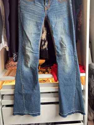 Blå bootcut jeans från True Religion - Säljer ett par blå bootcut jeans från True Religion med slitningar på framsidan och kontrastsömmar. Jeansen har klassiska fickor bak med den ikoniska hästsko-detaljen och knappstängning. Tvärt ramlade knapparna av och blev återställde med de man kan se på bilden. Perfekta för dig som gillar en avslappnad men ändå trendig look. Uppsprättade vid fötterna eftersom var lite korta på mig.