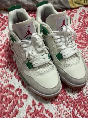 Vita och gröna Air Jordan 4 sneakers - Säljer ett par fräscha Air Jordan 4 sneakers i vitt med gröna detaljer och gummisula. Skorna har meshpaneler, klassisk snörning och Jumpman-logga på plösen. Perfekta för dig som vill sticka ut med stilrena och sportiga sneakers. Använda några gånger men är annars helt nya. Därför kör jag lite lägre pris på de. Storlek 46 på de. Men de passar för 45 också. Som är min storlek. Hör gärna av dig😁
