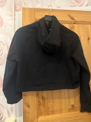 Svart cropped hoodie från ICANIWILL - Säljer en svart cropped hoodie från ICANIWILL med justerbar dragsko i nederkanten och liten vit logga på bröstet. Hoodien har långa ärmar och en klassisk huva. Perfekt till chill eller träning, riktigt skön och enkel att matcha.
