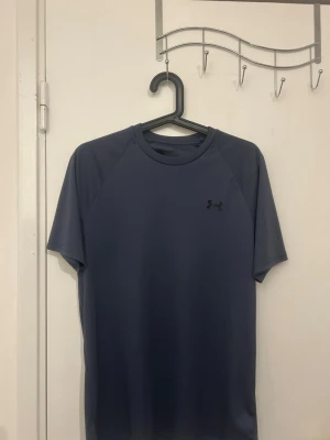 Blå tränings-tshirt från Under Armour - Snygg blå tränings-tshirt från Under Armour med rund hals och korta ärmar. Tillverkad i ett lätt och snabbtorkande funktionsmaterial som passar perfekt till gymmet eller löprundan. Diskret logga på bröstet.