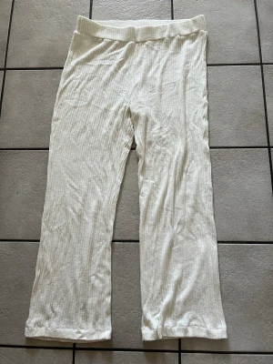 Vita ribbade loungebyxor storlek M/L - Mysiga loungebyxor i vitt med ribbad struktur och bred resår i midjan. Byxorna har raka ben och är tillverkade i ett mjukt, stretchigt material som passar perfekt för avslappnade dagar hemma.