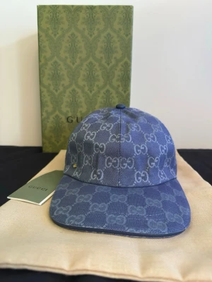 Blå GG-mönstrad keps - Säljer en blå keps i denim-look med det klassiska GG-monogrammet över hela kepsen. Kepsen har böjd skärm, justerbar rem bak och vita detaljer på insidan. Materialet är canvas med exklusiv känsla och kepsen kommer inte med en box