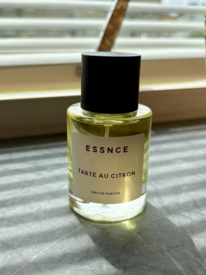 ESSNCE Tarte au Citron Eau de Parfum - Fräsch parfym från ESSNCE med doft av citronpaj. Flaskan är cylindrisk i genomskinligt glas med svart lock och vit etikett med svart text. Perfekt för dig som gillar fräscha och söta citrusdofter. Ny