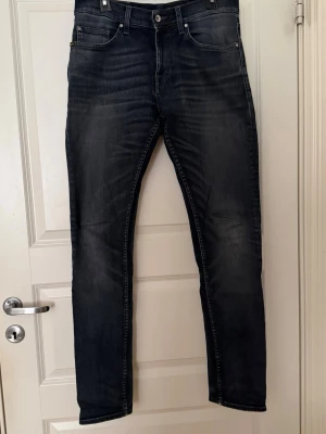 Mörkblå jeans från Tiger of Sweden - Snygga mörkblå jeans från Tiger of Sweden med slitningar och tvättade detaljer. Modellen är slim fit med klassisk femficksdesign och bälteshällor. Jeansen har dragkedjegylf och är tillverkade i denim med lite stretch för skön passform. Storlek 29/32, se lapp. 