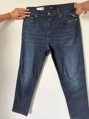 Mörkblå jeans från Replay - Säljer ett par mörkblå jeans från Replay, modell Sandot Relax Tapered. Klassisk femficksdesign med snygga kontrastsömmar och knappgylf. Jeansen har en avslappnad passform som smalnar av nedtill och är tillverkade i mjukt denimtyg.