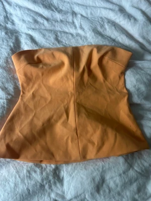 Orange axelbandslös tubtopp - Snygg orange tubtopp från Zara med figurnära passform och lätt utsvängd nederkant. Säljs inte längre på hemsidan. En knapp är påsydd men det är inget som syns! 