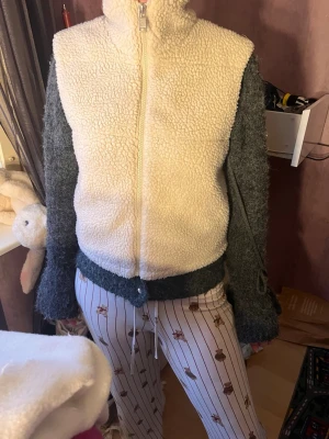 Off white teddyväst  med dragkedja - Mysig teddyväst i offwhite. Västen har hög krage och hel dragkedja framtill. Tillverkad i fluffigt teddy-material som ger en riktigt skön och trendig look.