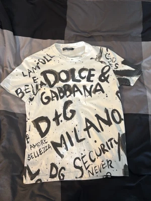Dolce & Gabbana t-shirt - Snygg vit t-shirt från Dolce & Gabbana med svart grafitti-inspirerat tryck över hela plagget. T-shirten har rund hals, korta ärmar och är tillverkad i mjuk bomull. Perfekt för dig som vill sticka ut med en unik och trendig look.