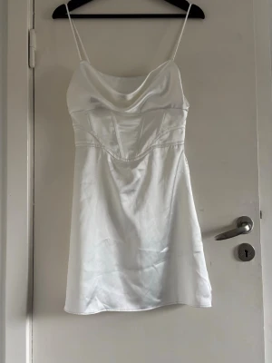 Vit satin kortklänning med smala band - Snygg vit kortklänning ifrån Zara i satin med tunna axelband och draperad urringning. Klänningen har en figurnära passform upptill och lätt utsvängd kjol. 
